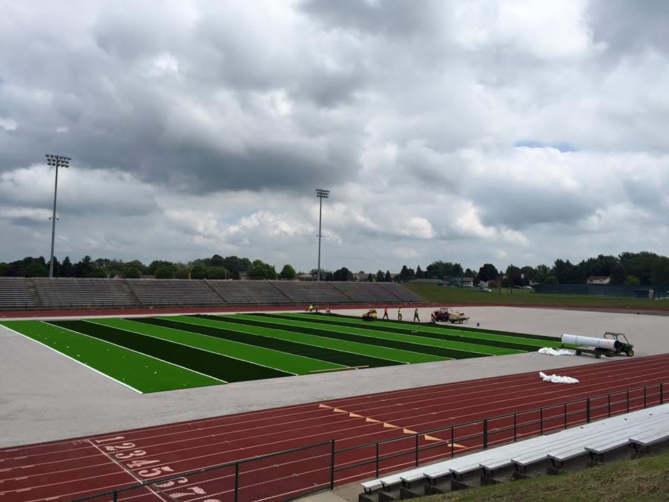 Rolls of synthetic turf being laid down on a stadium field